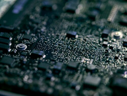 Close Up Of Electronic Circuit Board Of Laptop Being Repaired In Workshop With Low Key Lighting